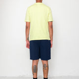 Person wearing a light yellow t-shirt and navy shorts against a white background