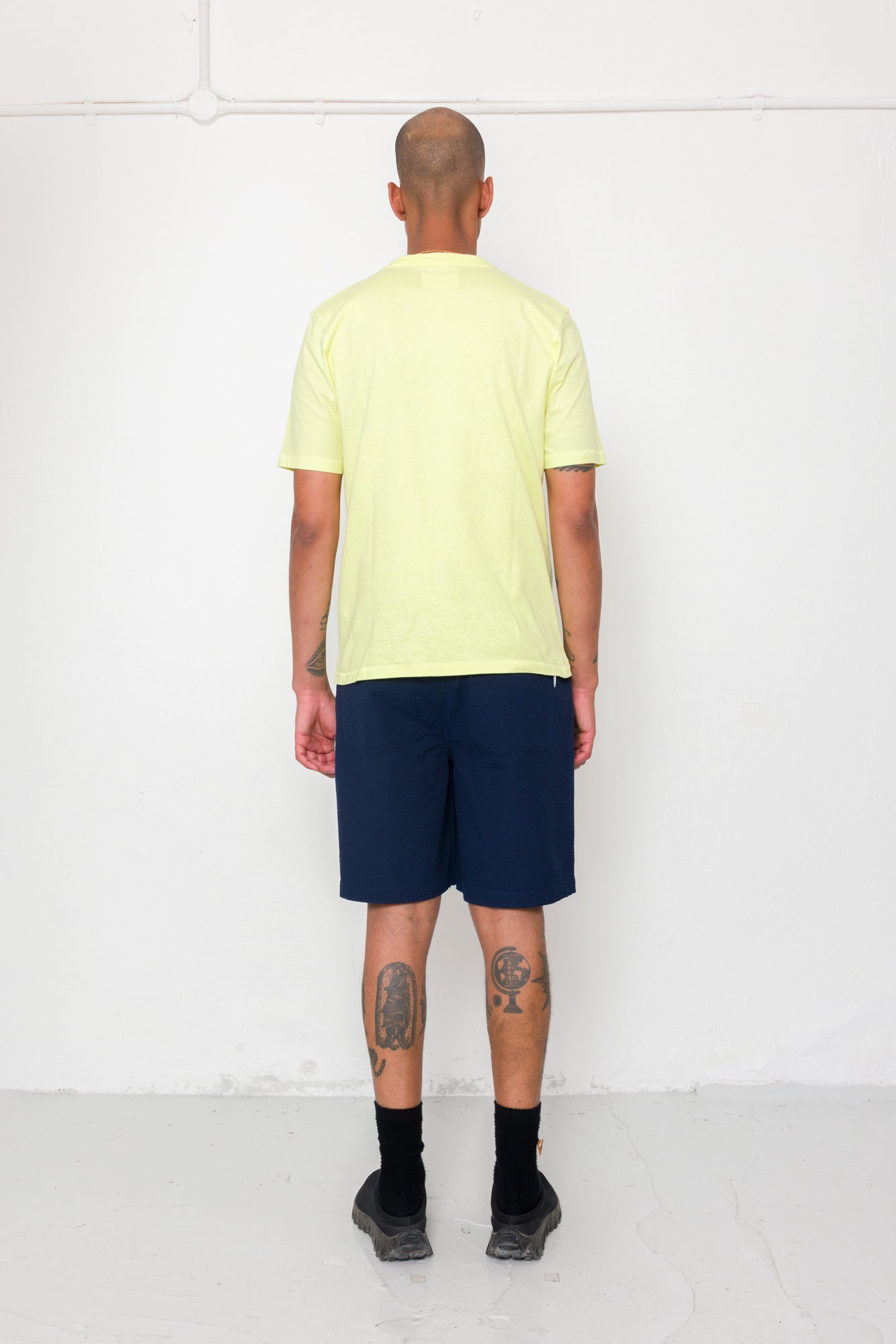 Person wearing a light yellow t-shirt and navy shorts against a white background