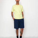 Man wearing a light yellow t-shirt and navy shorts against a white background