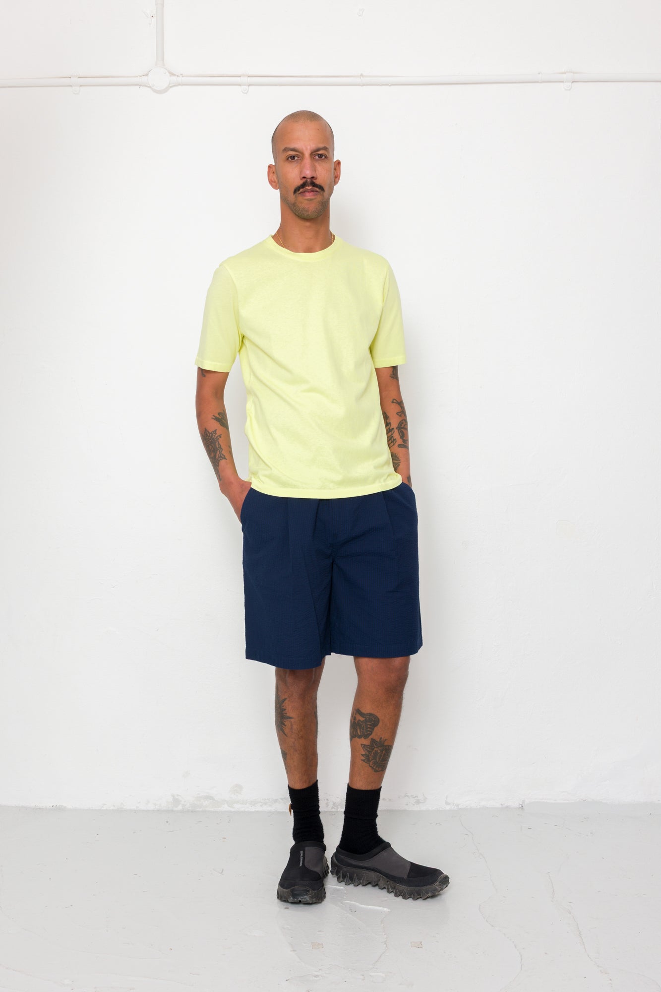 Man wearing a light yellow t-shirt and navy shorts against a white background