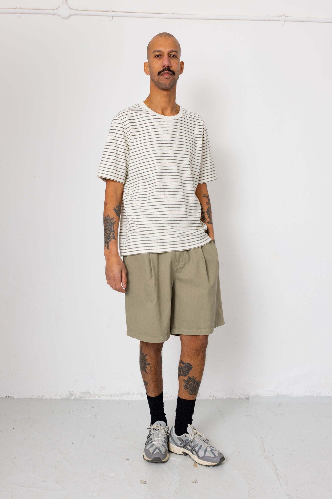 Man wearing striped t-shirt and beige shorts in front of white wall