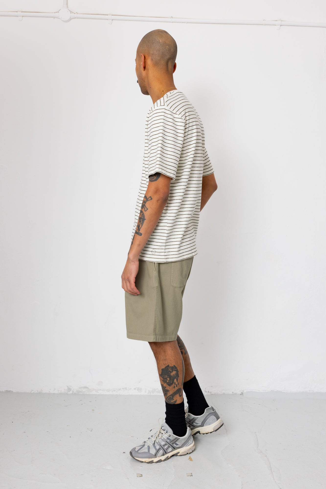 Man wearing striped t-shirt and beige shorts in front of white wall