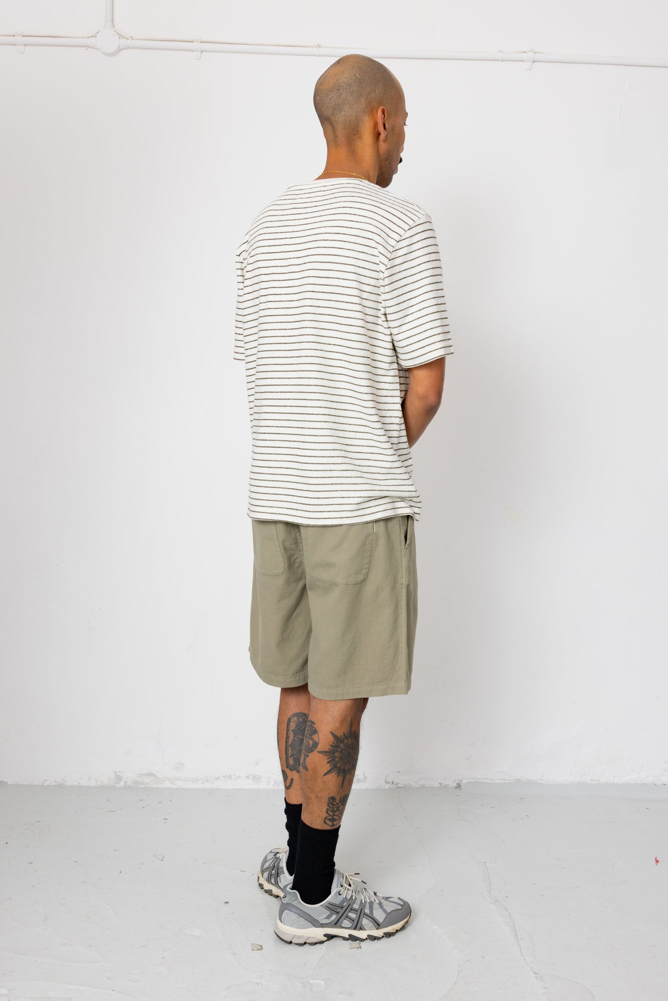Man wearing striped t-shirt and beige shorts in front of white wall