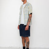Man wearing a plaid shirt, white t-shirt, denim shorts, and black boots against a white background