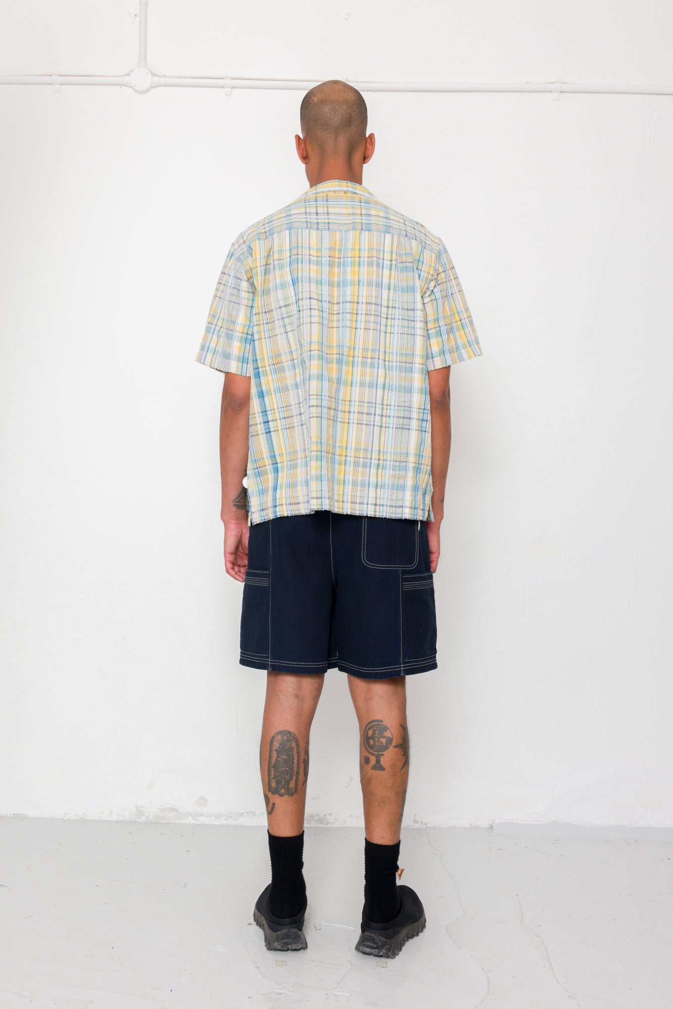 Person wearing a plaid shirt and dark shorts against a white background