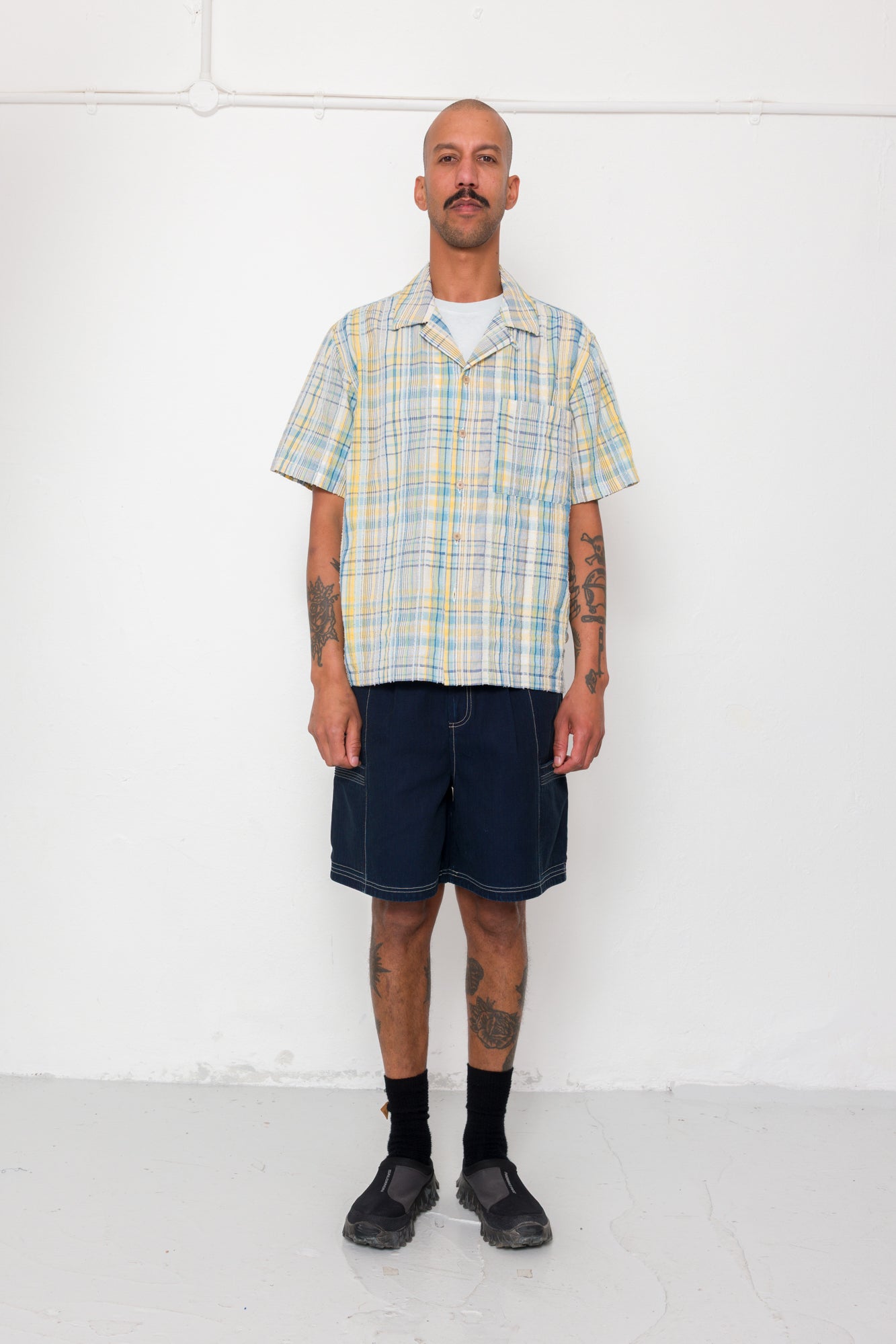 Man wearing a plaid shirt and dark shorts against a white background