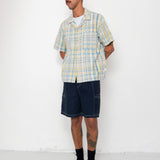 Man wearing a checkered shirt and dark shorts against a white background