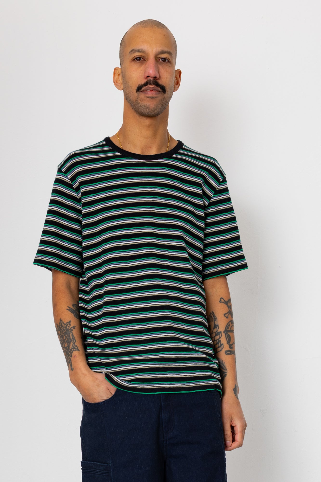 Man wearing dark coloured striped t-shirt and navy shorts against light grey background