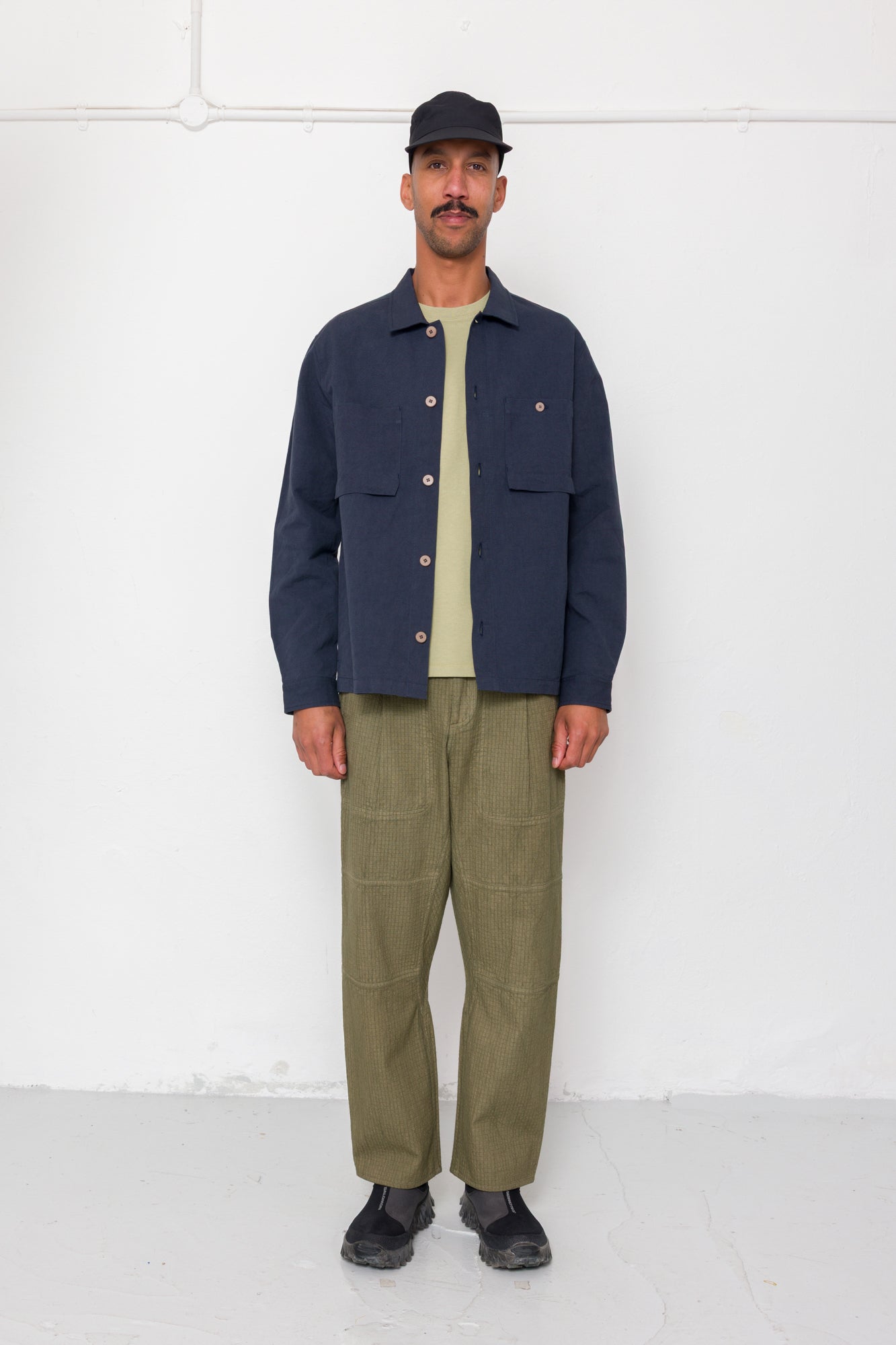 Man wearing a navy jacket, beige shirt, and green pants against a white background