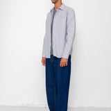 Man wearing a light gray shirt and dark blue pants against a white background