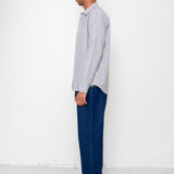 Man wearing a light gray shirt and dark blue jeans standing against a white wall.