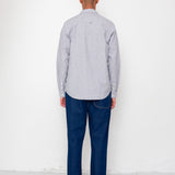 Man wearing a light gray shirt and dark blue jeans standing against a white wall.