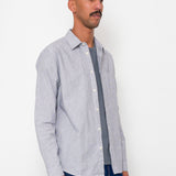 Man wearing a light gray button-up shirt over a dark gray t-shirt with blue pants against a white background