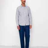 Man wearing a light gray button-up shirt and dark blue pants against a white background