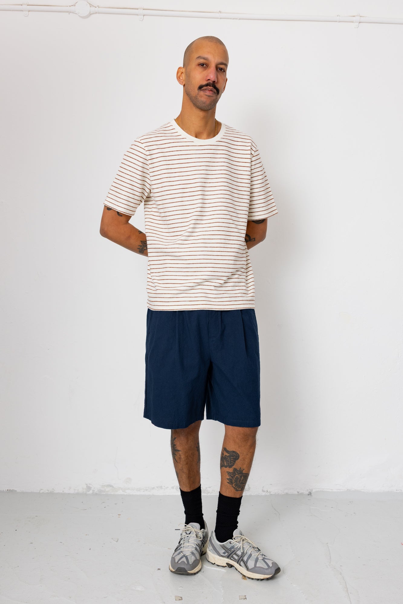 Man wearing a striped shirt and navy shorts against a white background