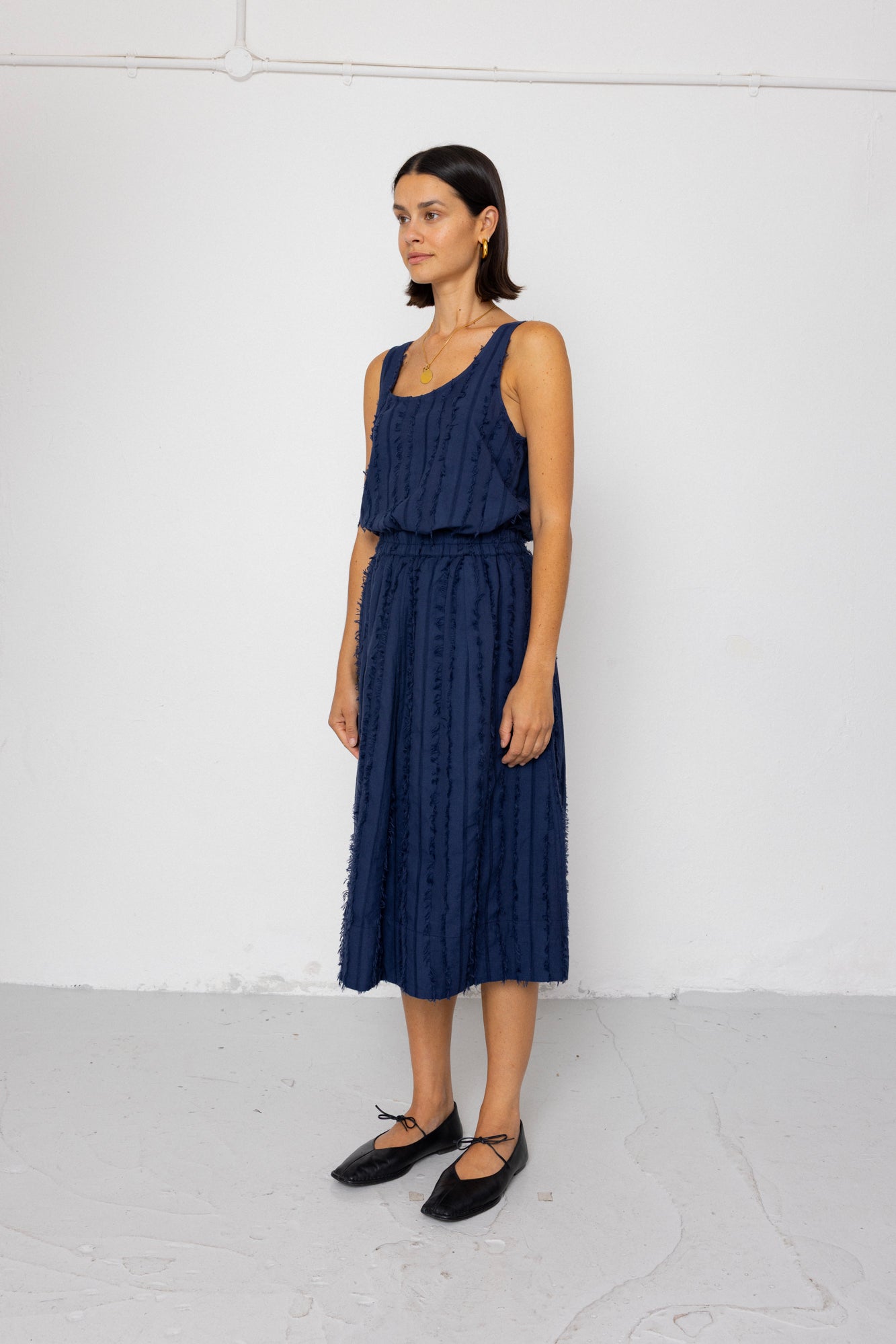 Woman wearing a navy blue sleeveless top and textured skirt against a white background