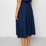 Woman wearing a navy blue sleeveless top and textured skirt against a white background