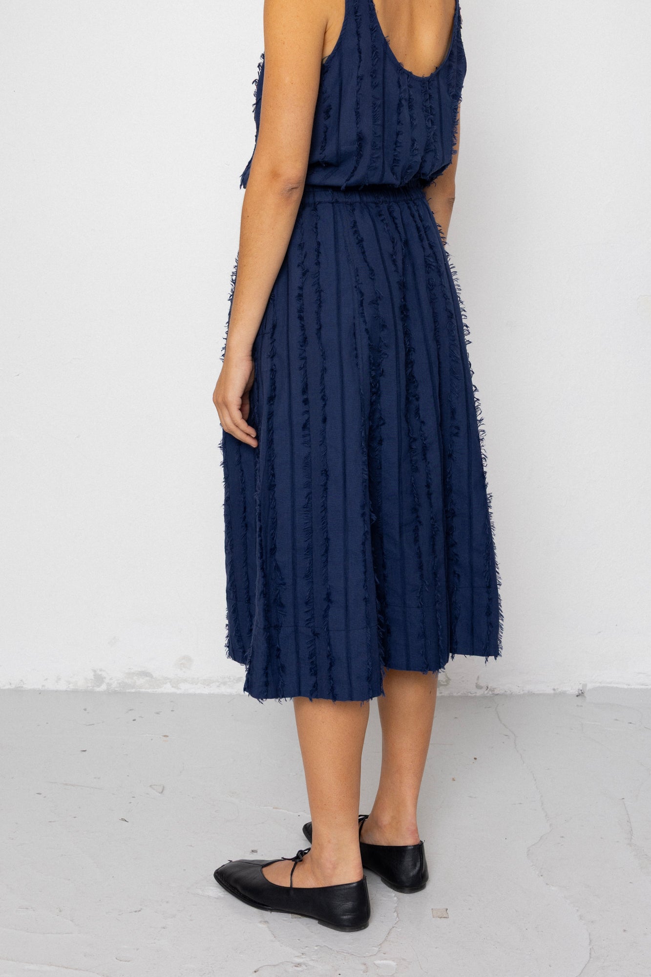 Woman wearing a navy blue sleeveless top and textured skirt against a white background
