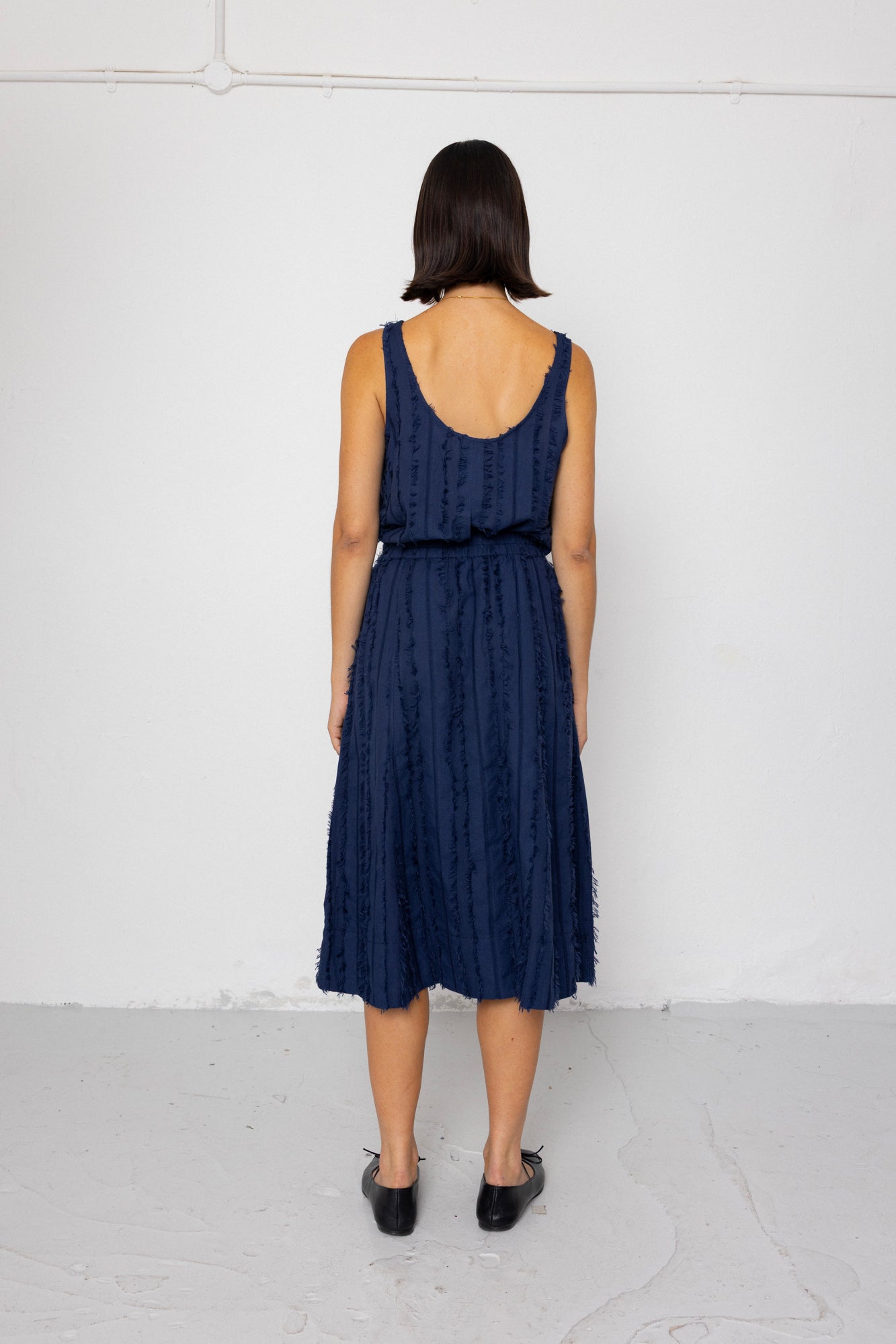 Woman wearing a navy blue sleeveless top and textured skirt against a white background
