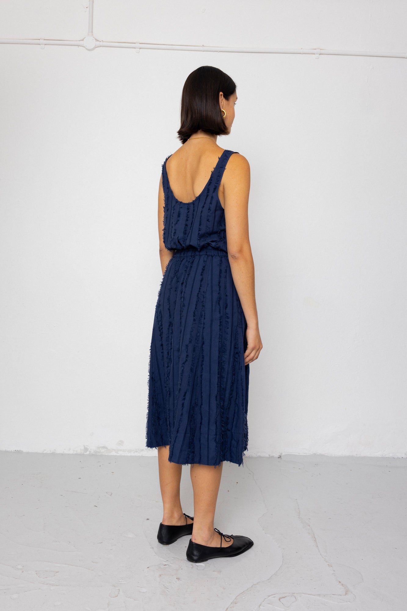 Woman wearing a navy blue sleeveless top and textured skirt against a white background