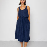 Woman wearing a navy blue sleeveless top and textured skirt against a white background
