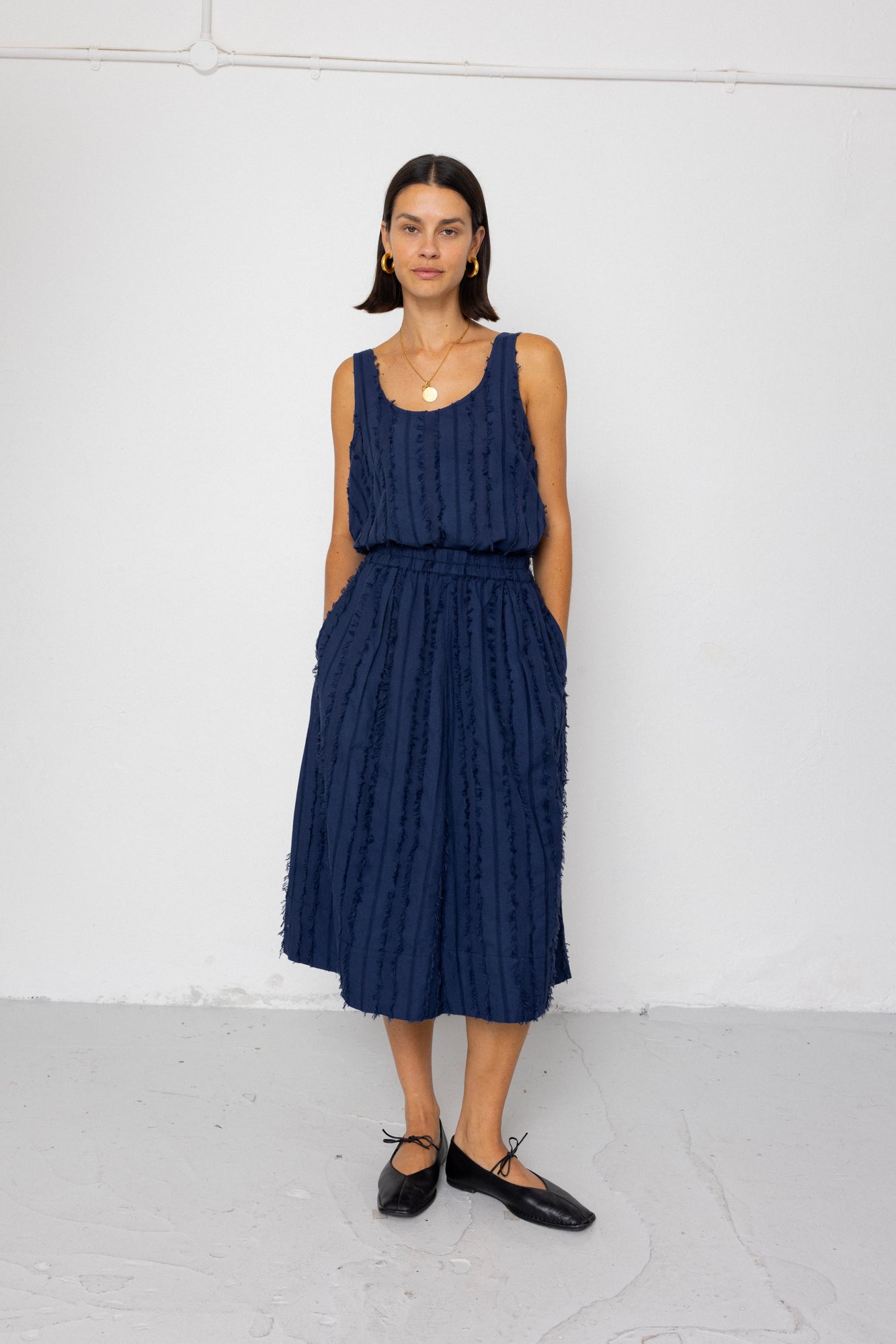 Woman wearing a navy blue sleeveless top and textured skirt against a white background