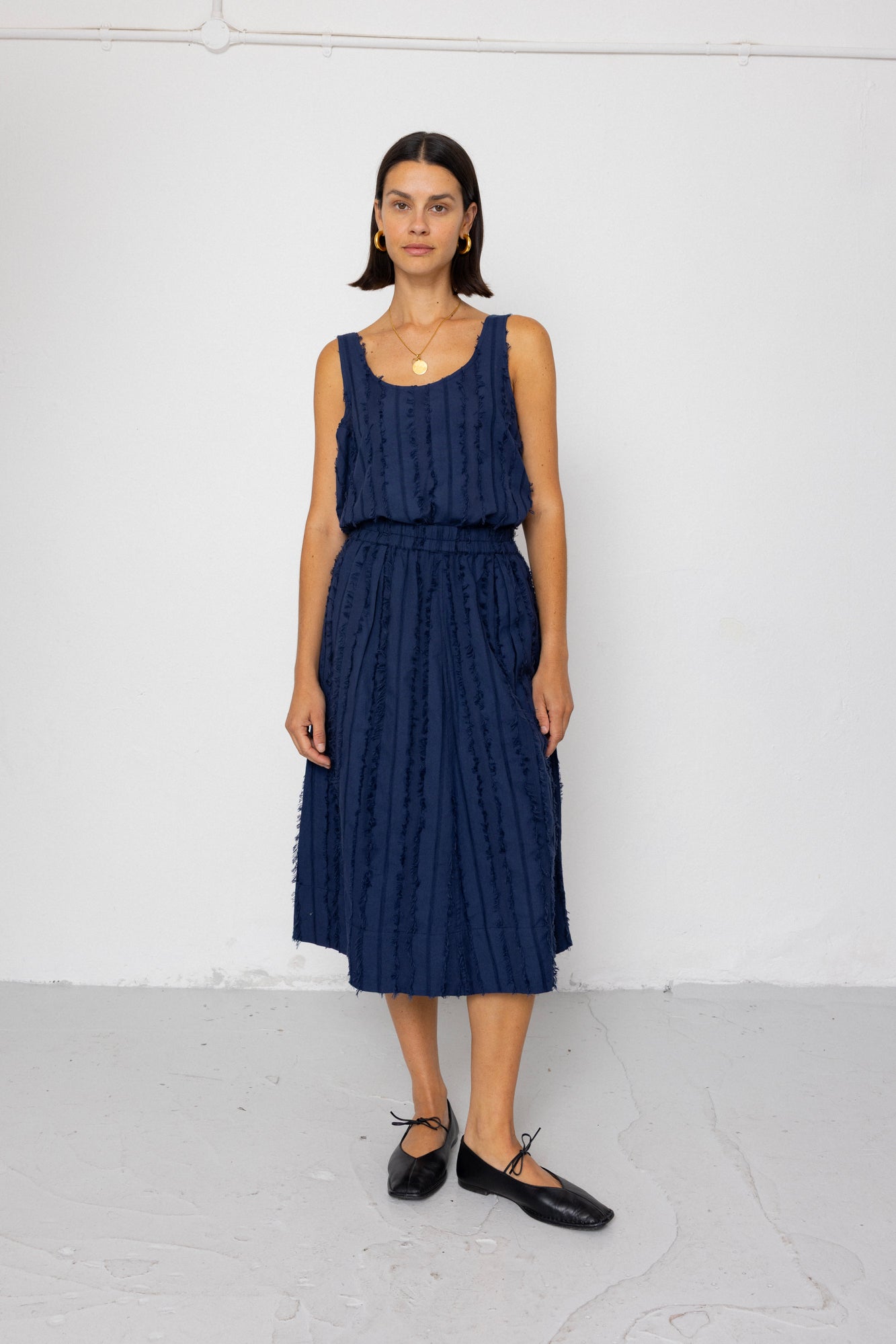 Woman wearing a navy blue sleeveless top and skirt set against a white background