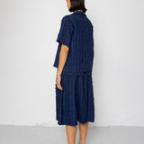 Person wearing a navy textured outfit standing against a white wall.