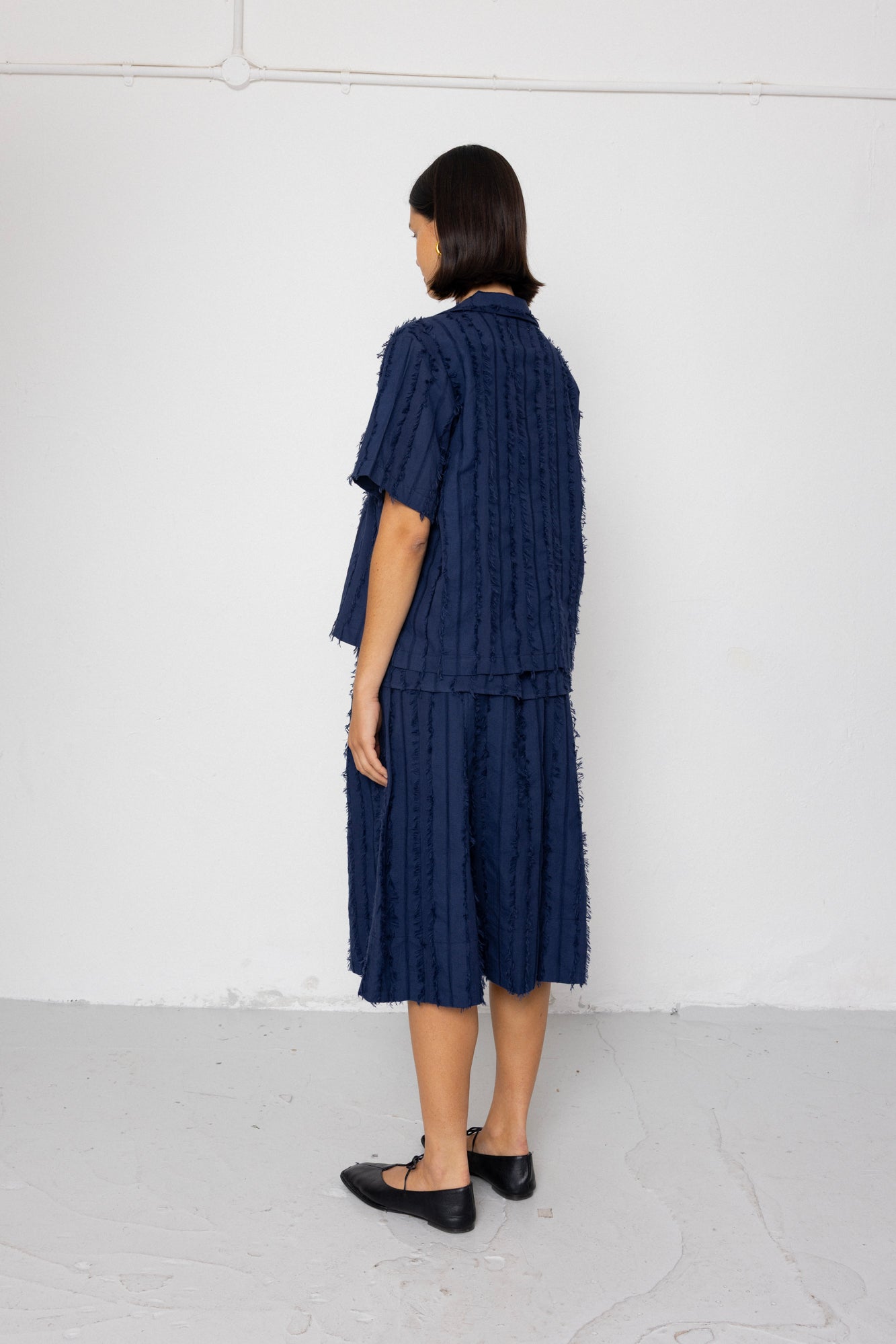 Person wearing a navy textured outfit standing against a white wall.