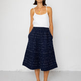 Woman wearing a white tank top and navy skirt against a white background