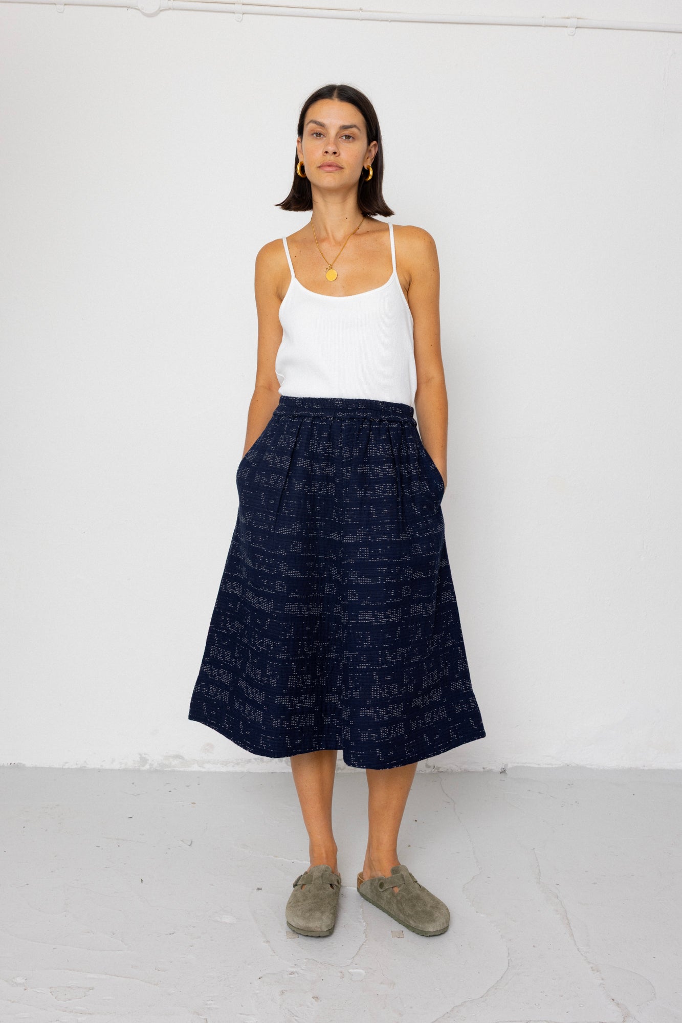 Woman wearing a white tank top and navy skirt against a white background