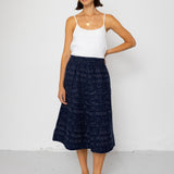 Woman wearing a white tank top and navy patterned skirt on a white background