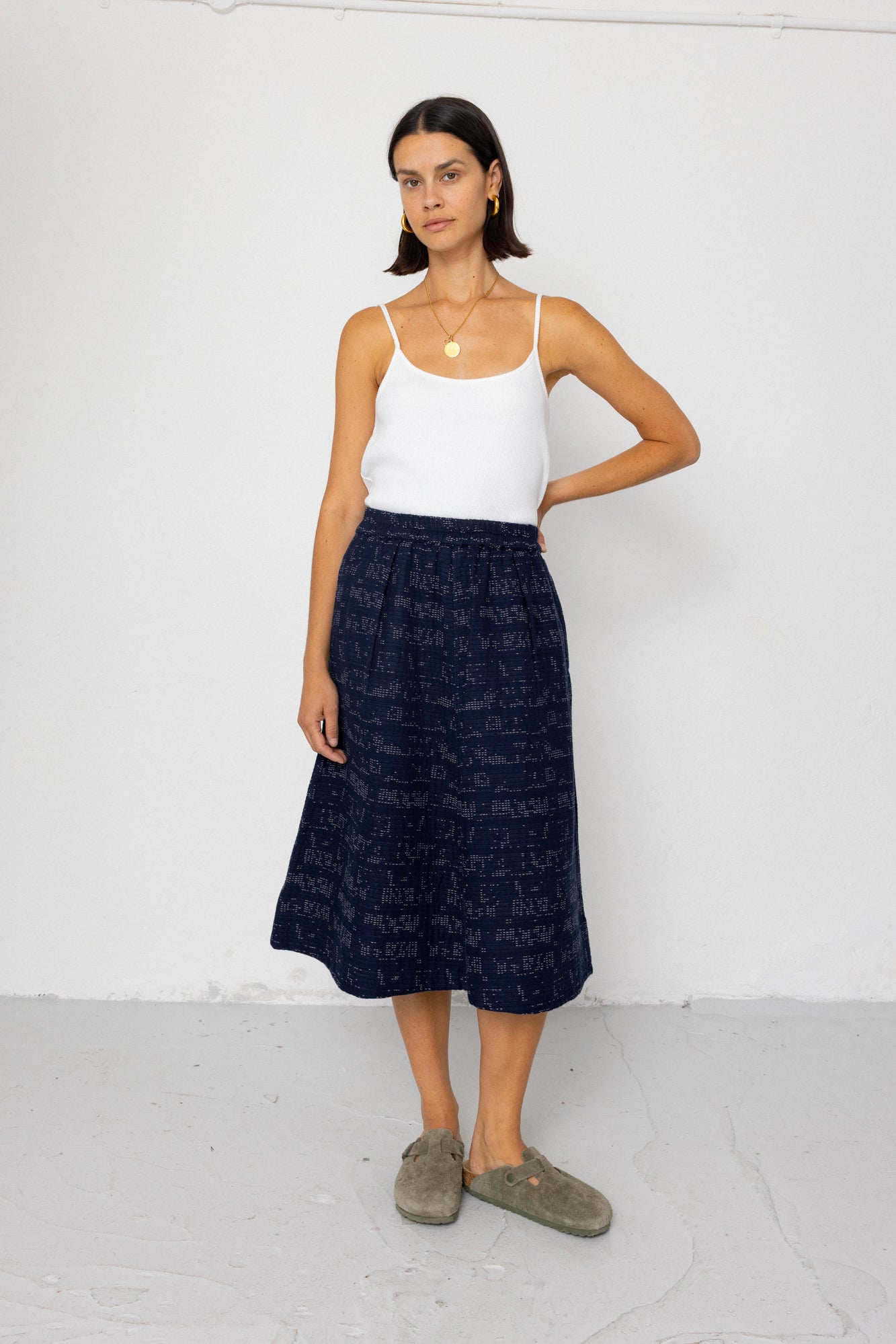 Woman wearing a white tank top and navy patterned skirt on a white background