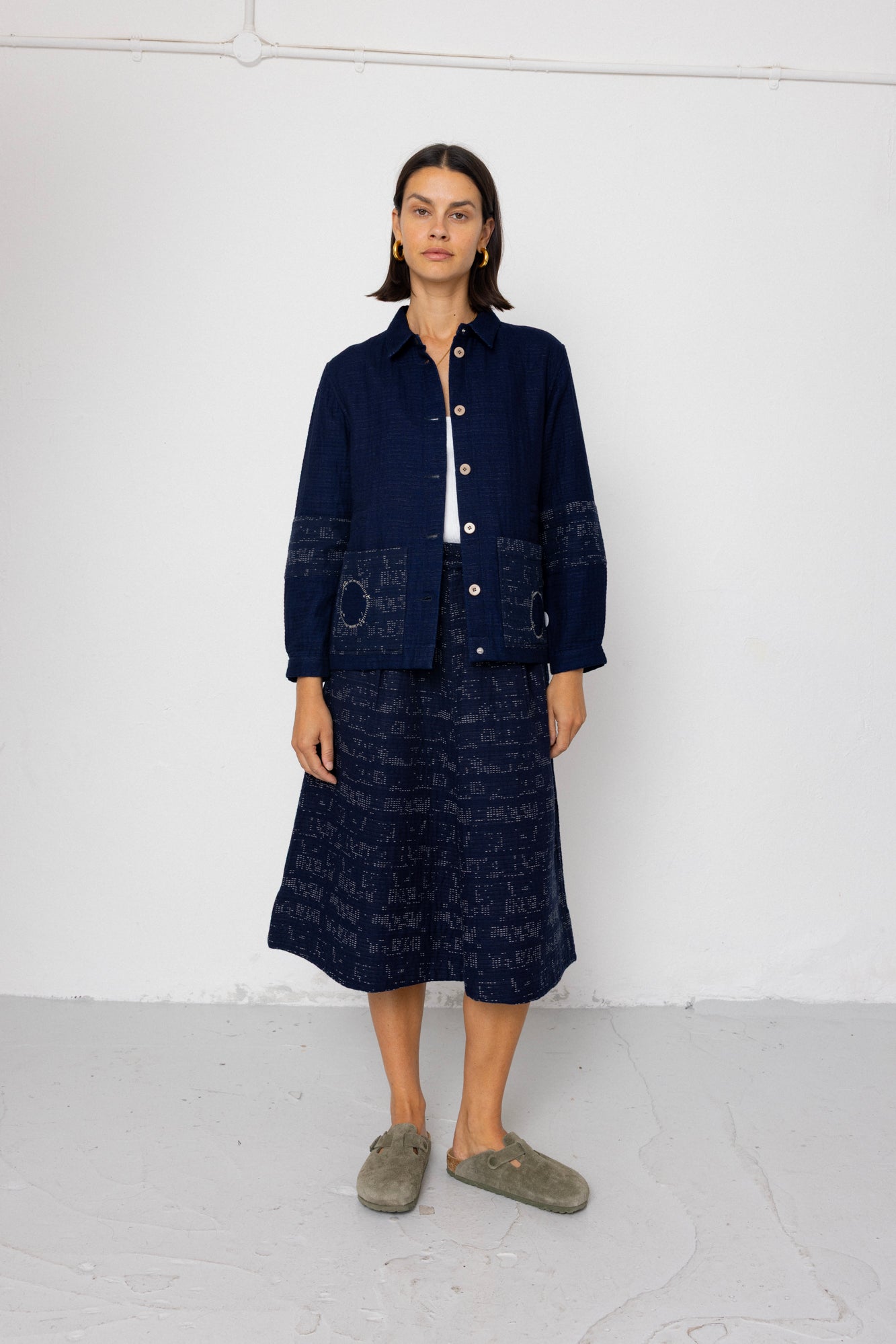 Person wearing a dark blue outfit with a jacket and skirt on a white background
