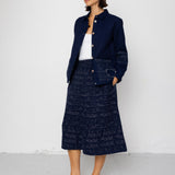 Woman wearing a navy blue textured coat and skirt against a white background
