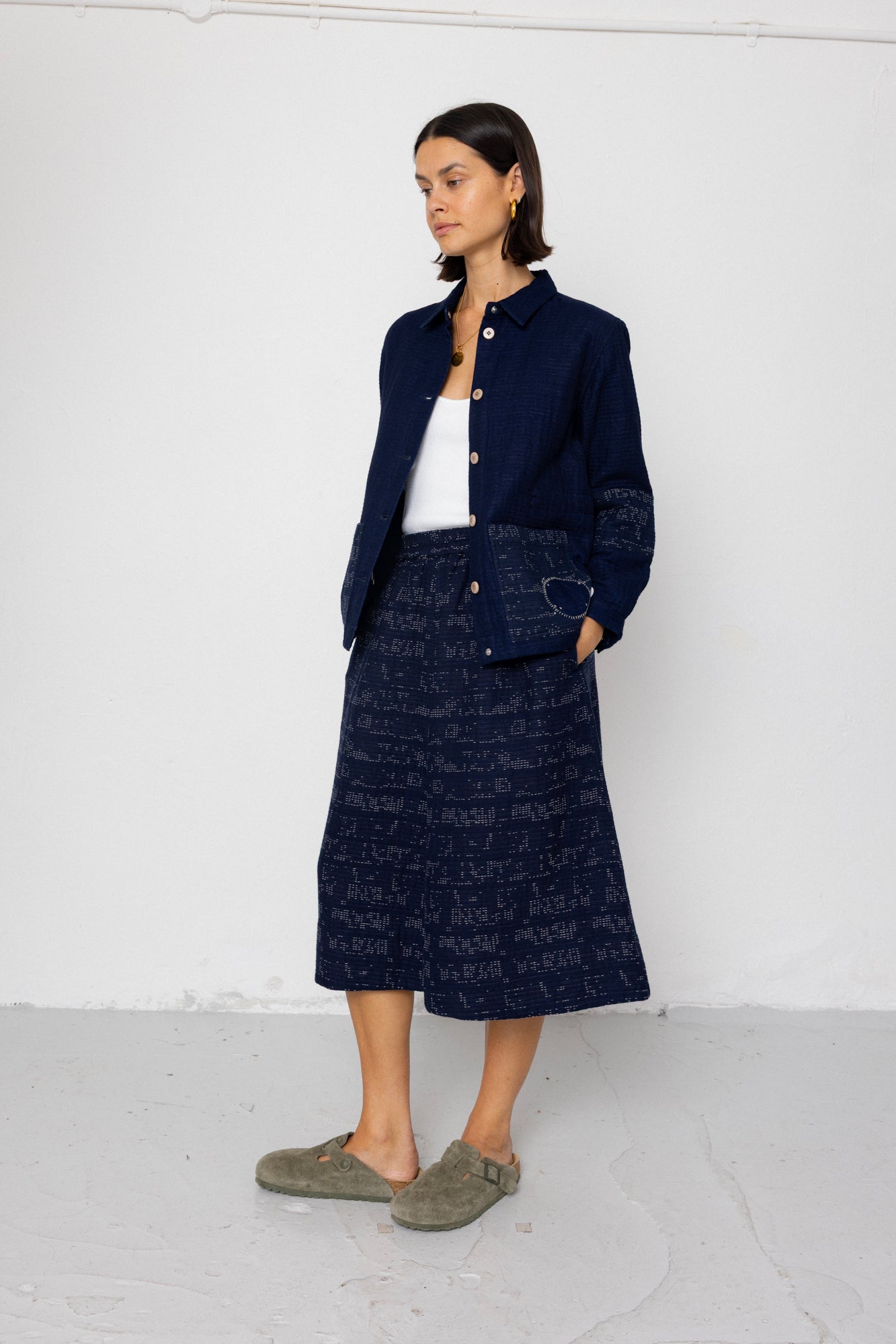 Woman wearing a navy blue textured coat and skirt against a white background