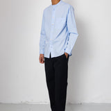 Man wearing a light blue shirt and black pants against a white background