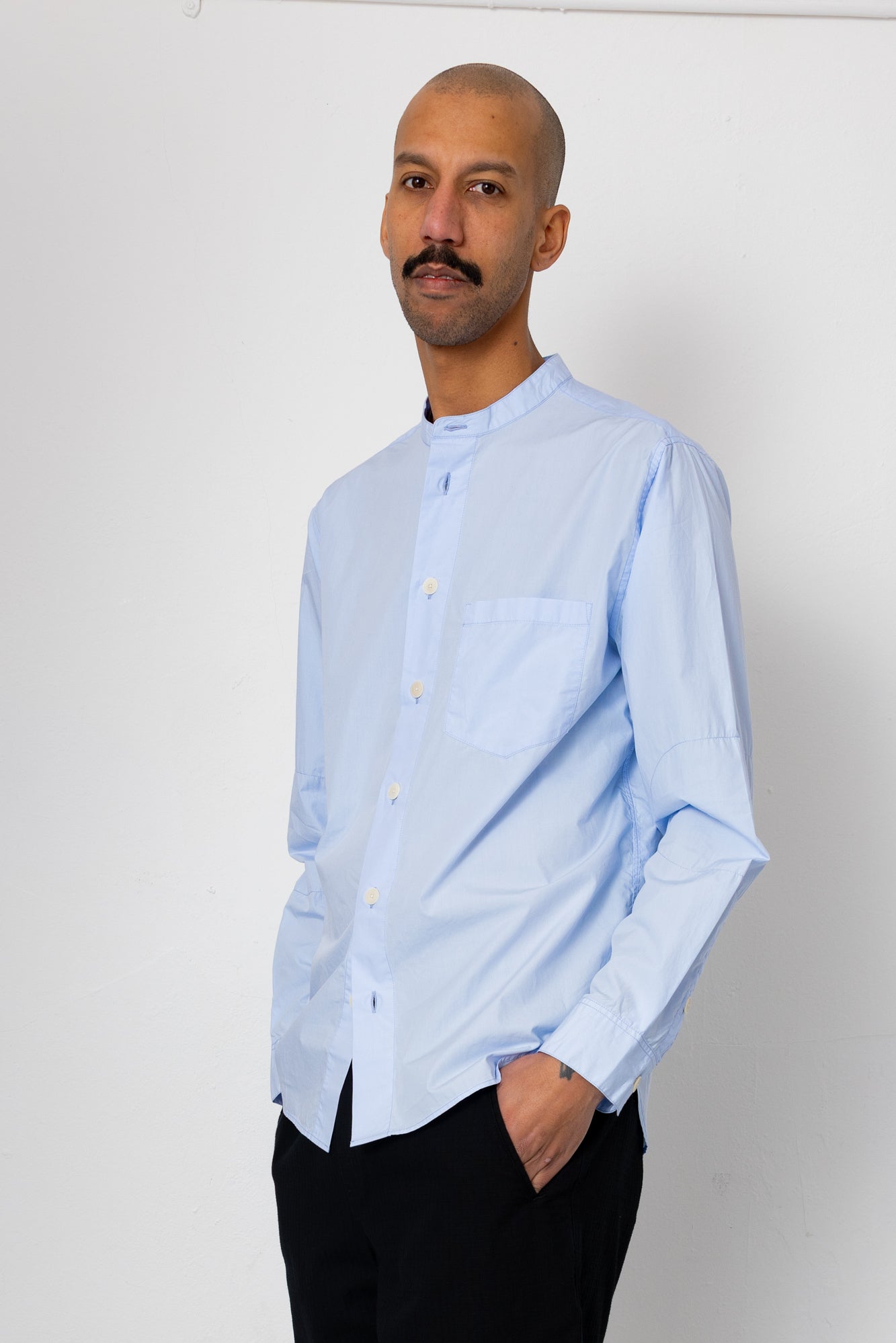 Man wearing a light blue shirt and black pants against a white background