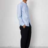 Man wearing a light blue shirt and black pants against a white background