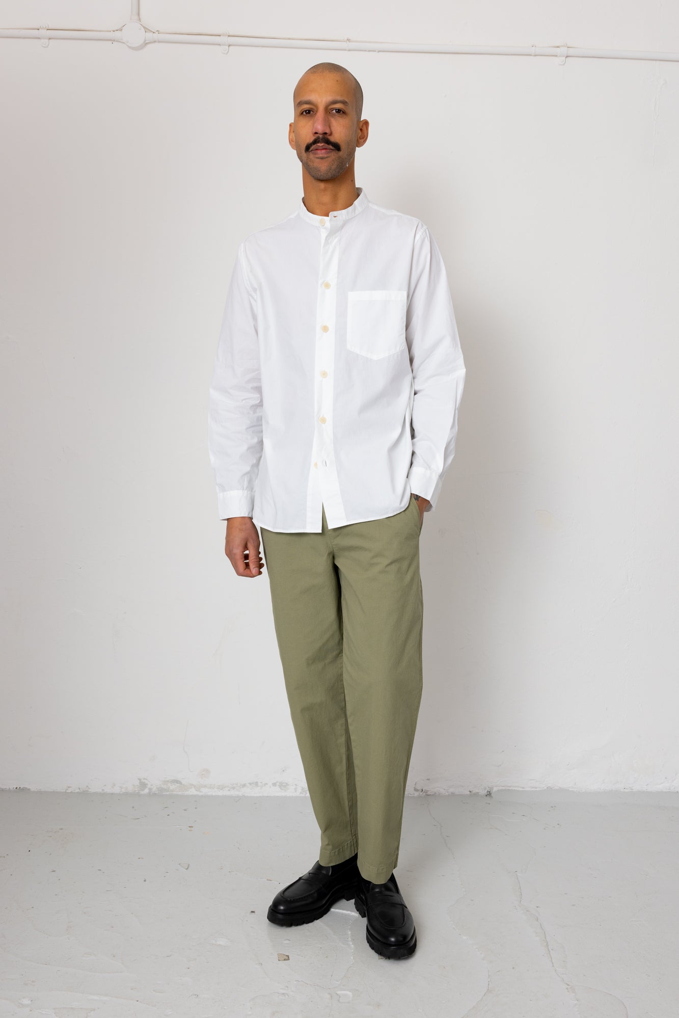 Man wearing a white shirt and green pants against a white background