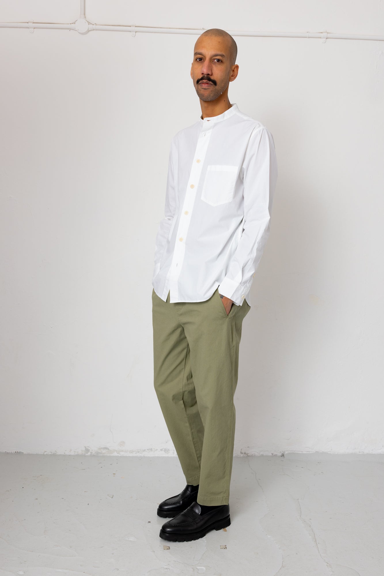 Man wearing a white shirt and green pants against a white background