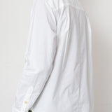 Person wearing a white button-up shirt and green pants against a plain background