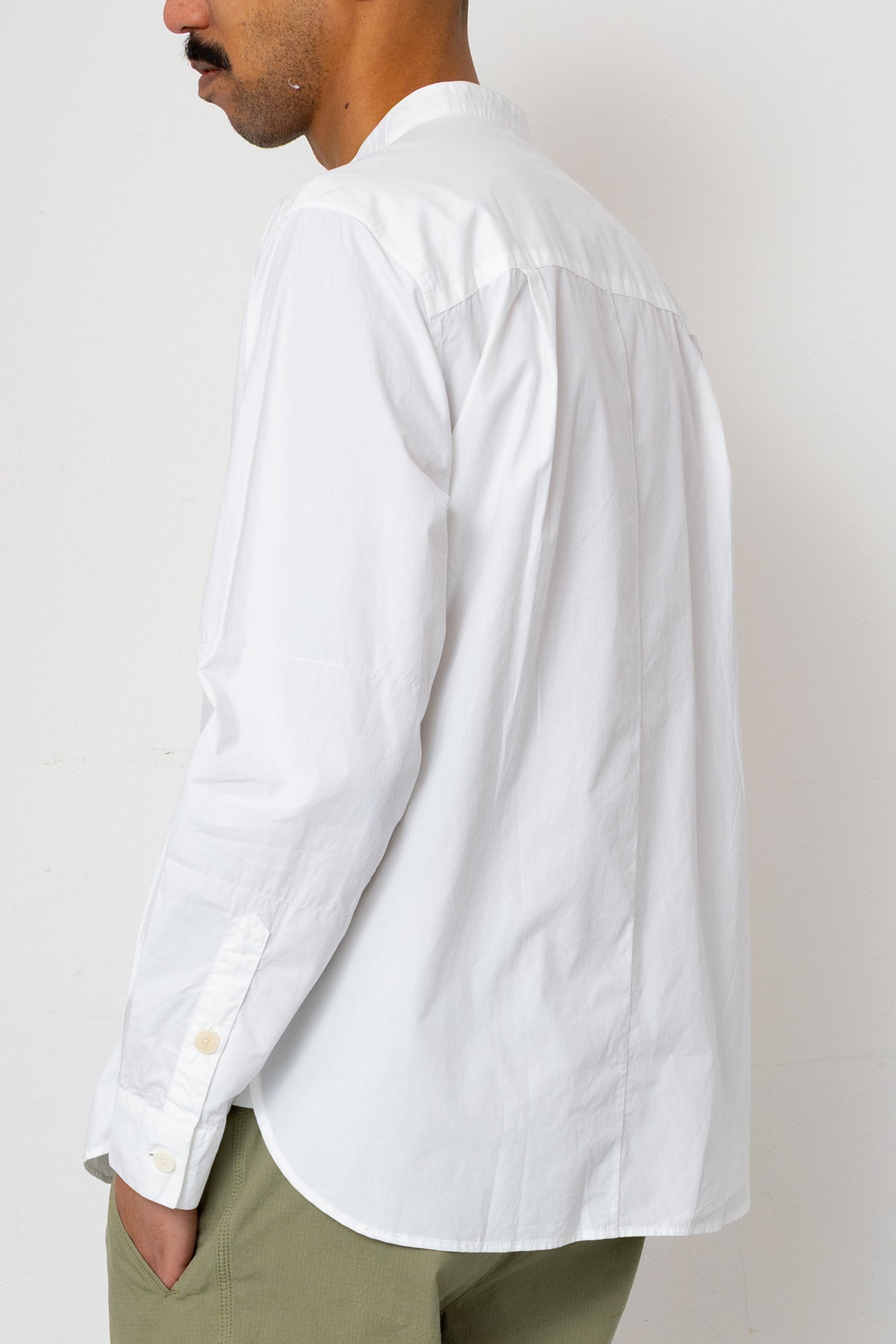 Person wearing a white button-up shirt and green pants against a plain background