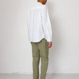 Person wearing a white shirt and green pants against a white wall
