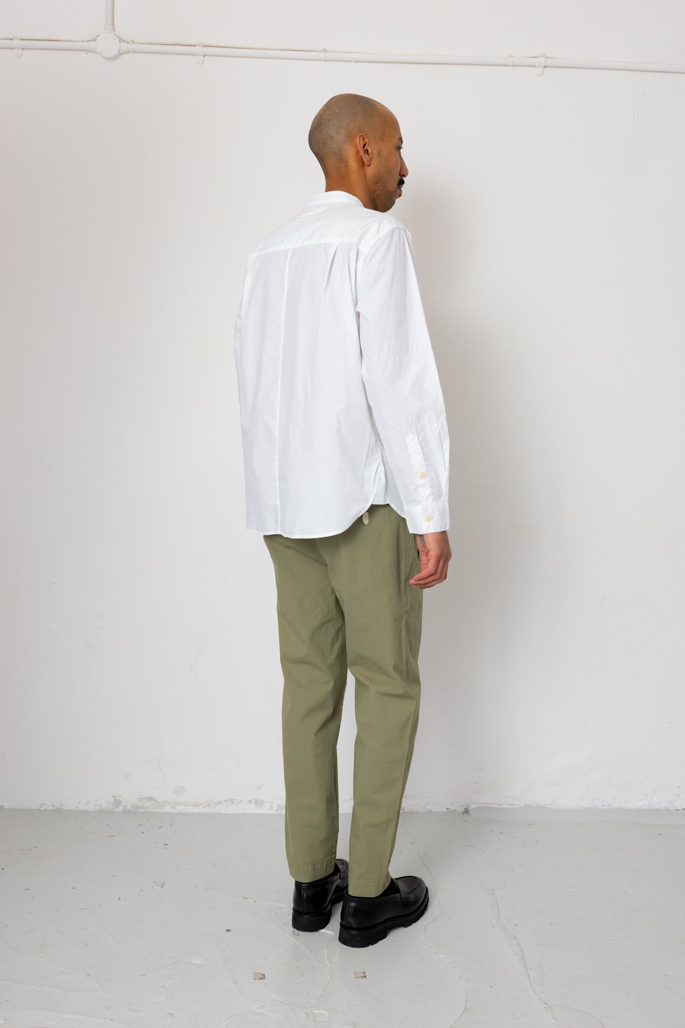 Person wearing a white shirt and green pants against a white wall