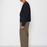Man wearing a black quilted jacket, green pants, and a cap against a white background