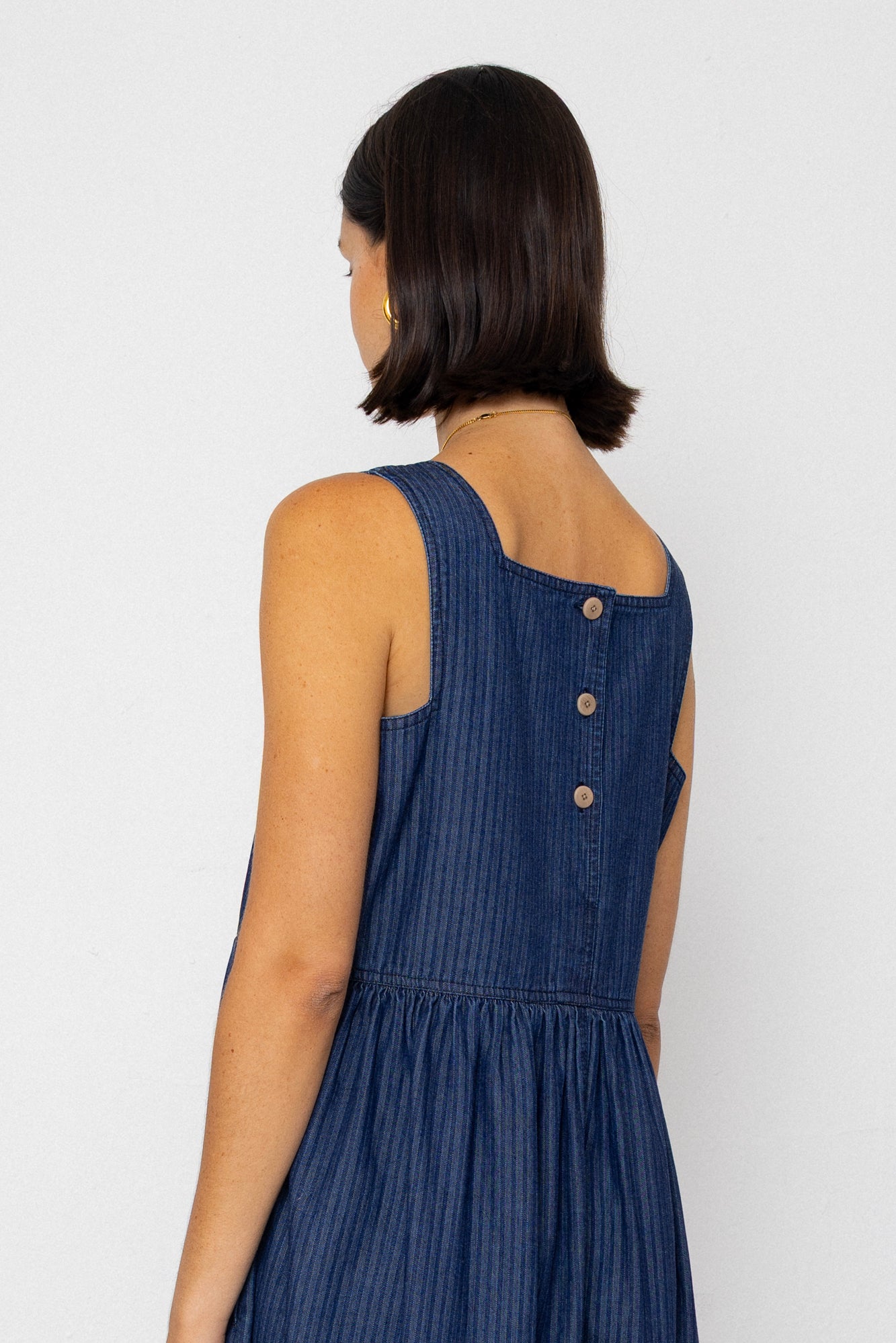 Woman wearing a blue striped denim dress with button details on a white background