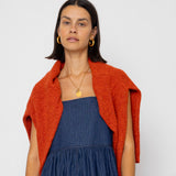 Woman wearing a blue dress and orange cardigan against a white background