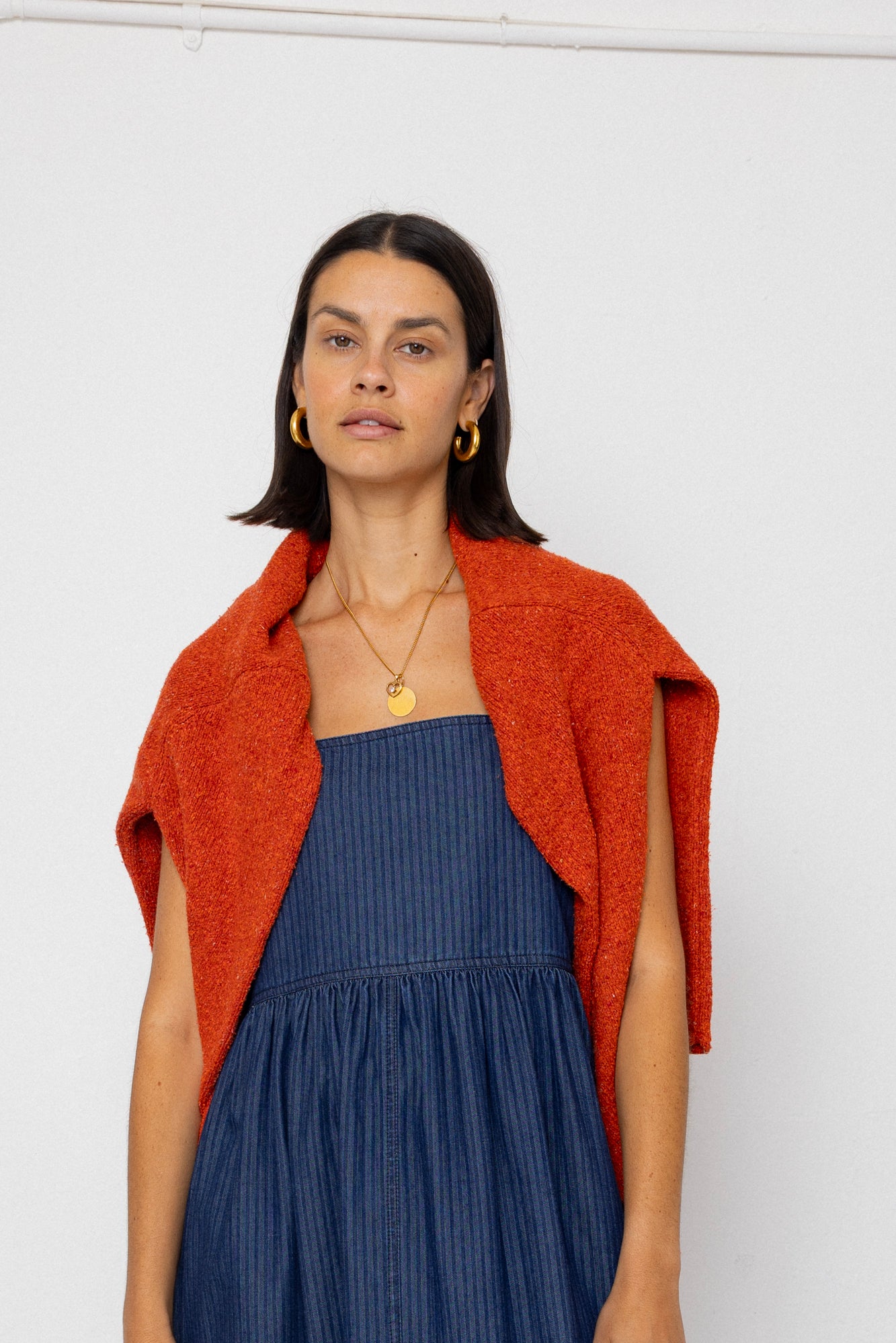 Woman wearing a blue dress and orange cardigan against a white background