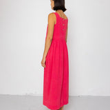 Woman wearing a pink dress with buttons on the back against a white background